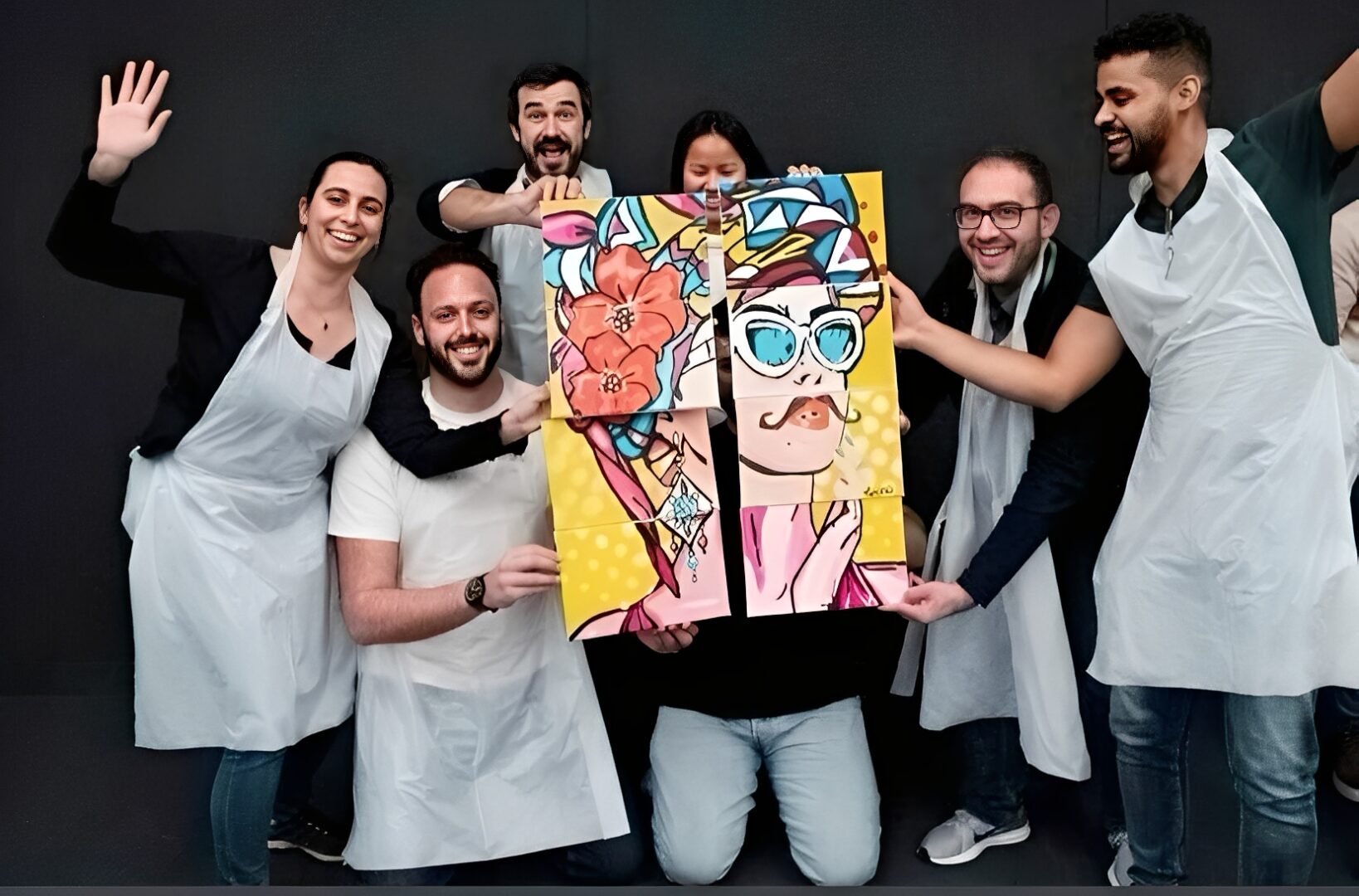 Group holding colorful artwork, wearing aprons.