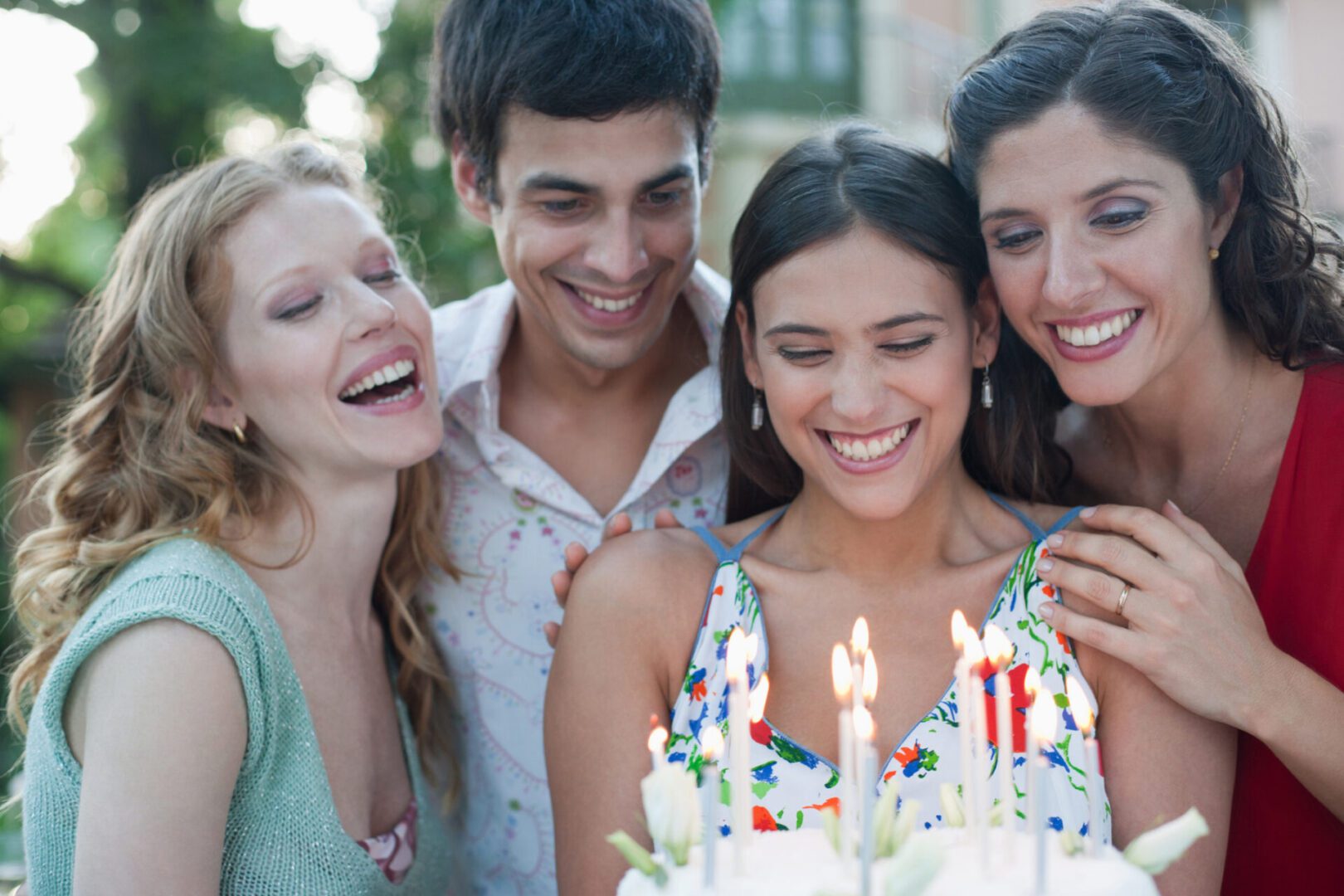 Four people with birthday cake at a party outdoors smiling